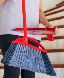Woman with broom & dust pan cleaning staircase at home while doing chores around the house